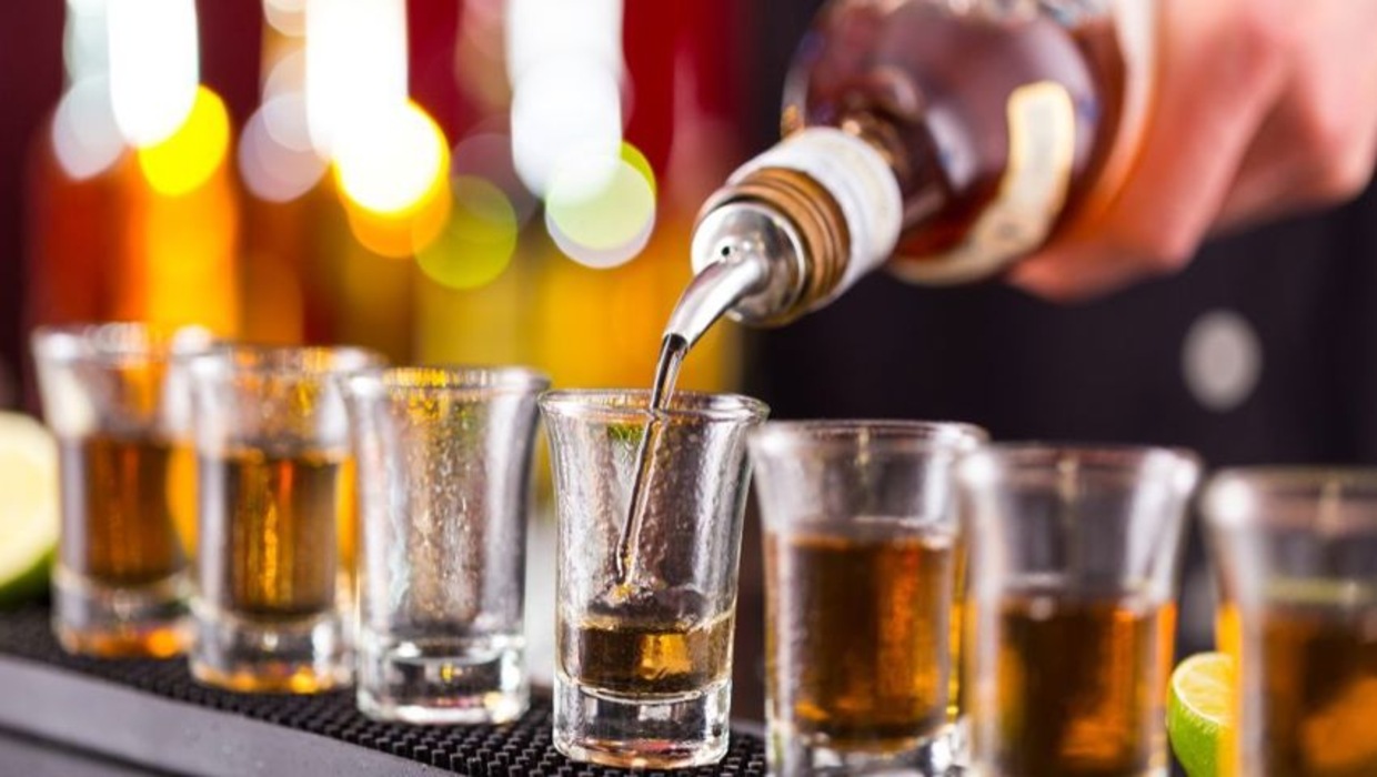queensland-events Bartender pouring spirits into a row of shot glasses at a bar, capturing the nightlife feel of queensland events