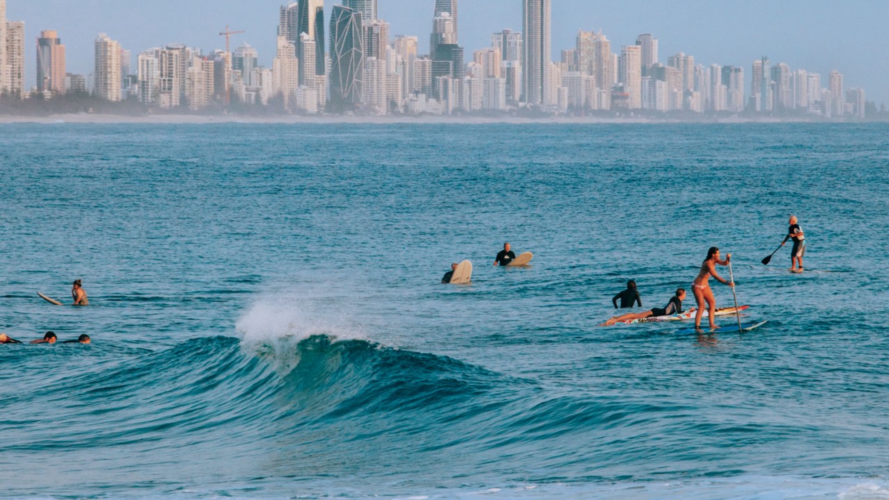 walkable-broadbeach-from-koko Surfers and paddleboarders off Broadbeach with the Gold Coast skyline behind, near Koko Broadbeach